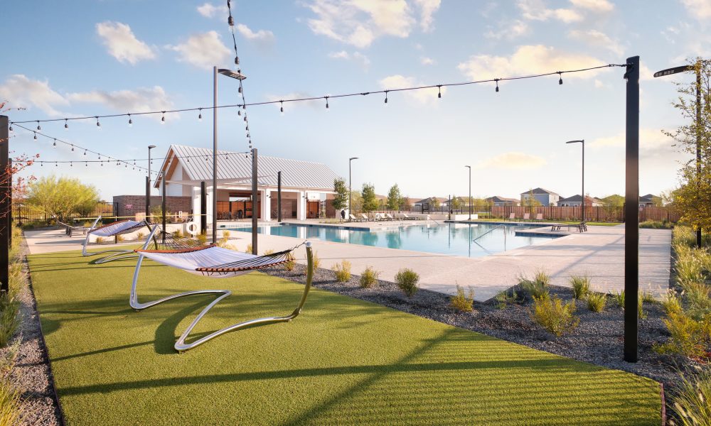 Photo of amenity center in Brohn Homes Hymeadow in Maxwell, TX. Free-standing hammocks in grass with string lights above. Pool and building in background.