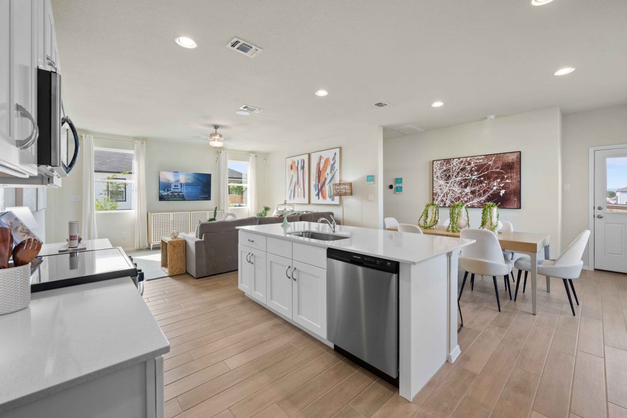 An interior image of a kitchen with white marble counter top and island, vinyl flooring, white cabinets, and steel refrigerator and dishwashers and a black and steel stove.