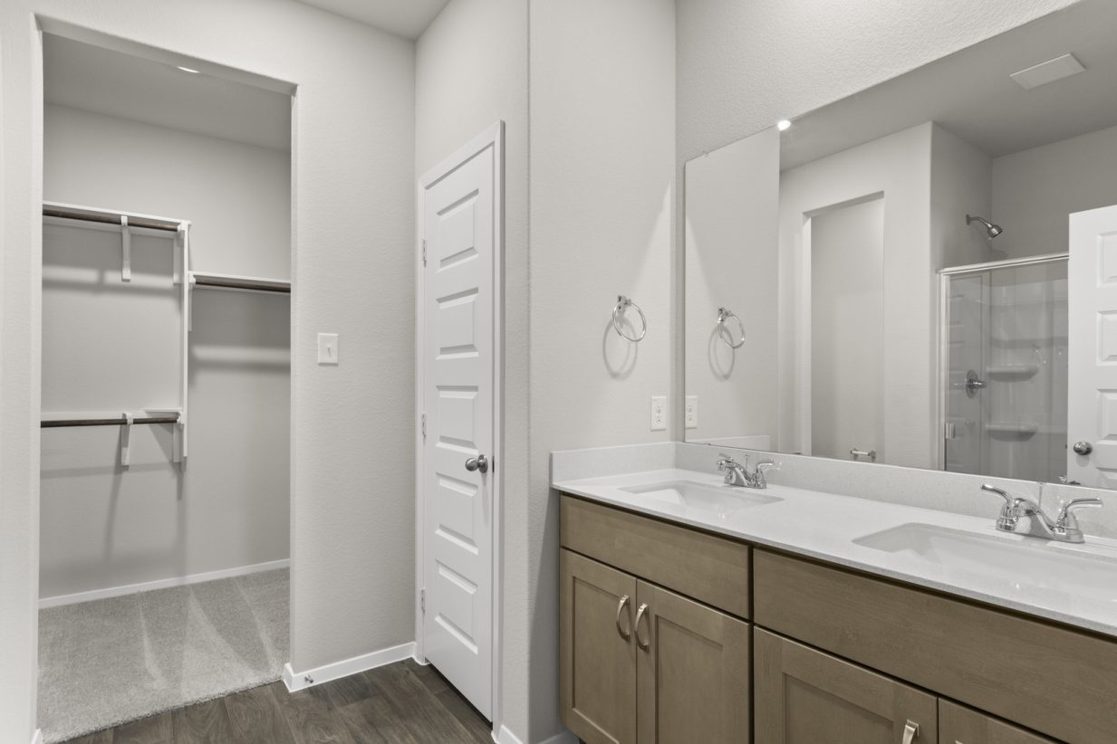 Image of primary bathroom with light brown cabinets and a large mirror with vanity and a connected closet