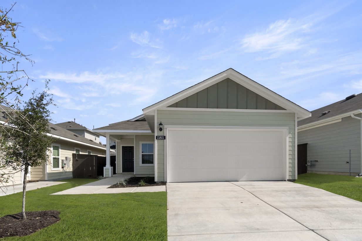 Image of a green one story home exterior with a back front door with a white two car garage and a cement driveway with green grass and a blue sky