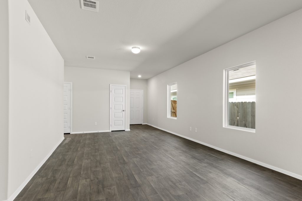 Image of a one story home living room with dark wood-like flooring and light grey painted walls with two windows