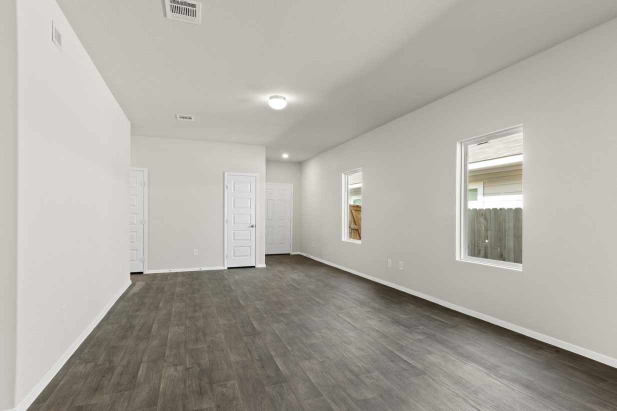 Image of a one story home living room with dark wood-like flooring and light grey painted walls with two windows