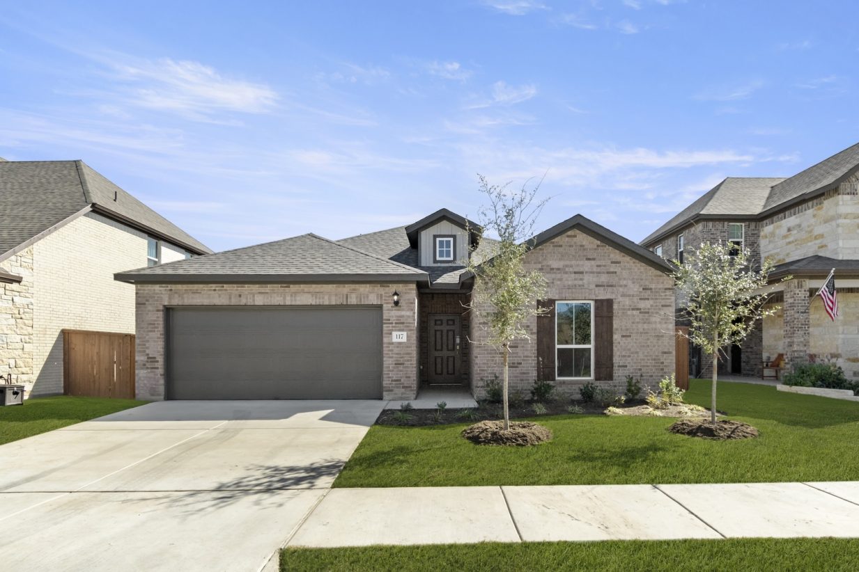 Image of the exterior of a one story brick home qith a brown two car garage and a cement driveway, a green grass front yard and a blue sky in the background