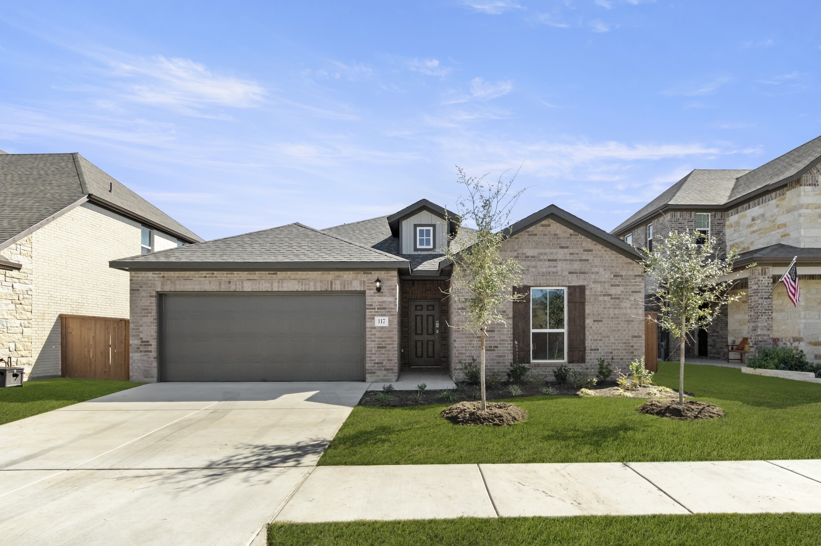 Image of the exterior of a one story brick home qith a brown two car garage and a cement driveway, a green grass front yard and a blue sky in the background