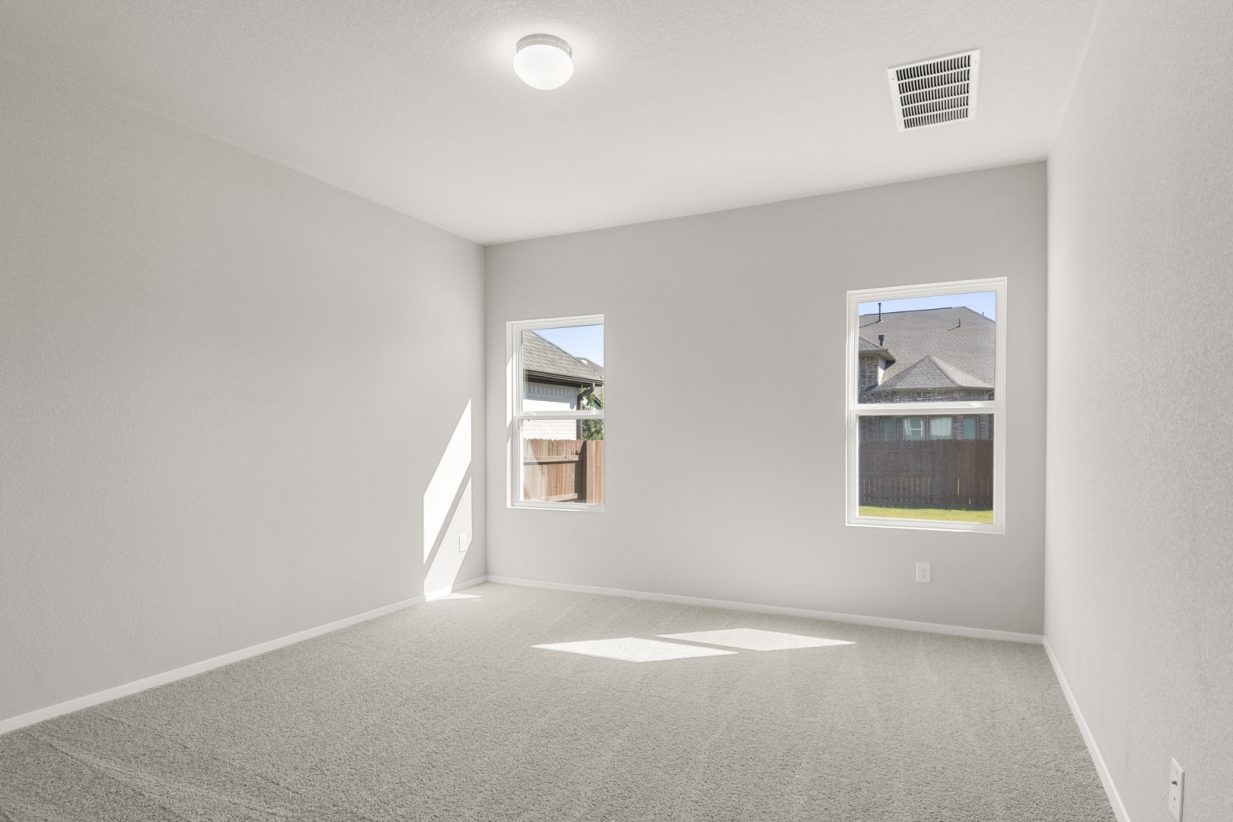 Image of a primary bedroom with tan carpeting, light grey walls, and two windows