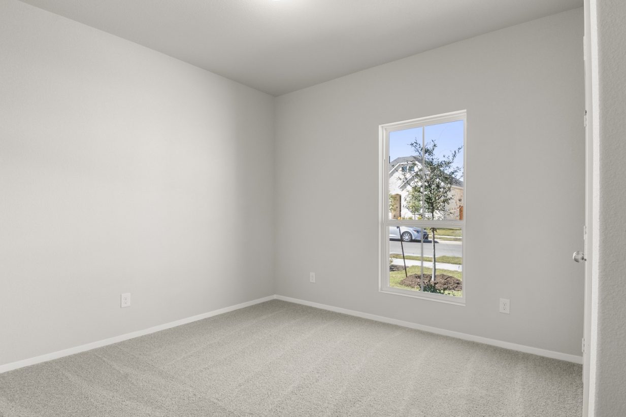 Image of a bedroom with tan carpeting and light grey walls with a window