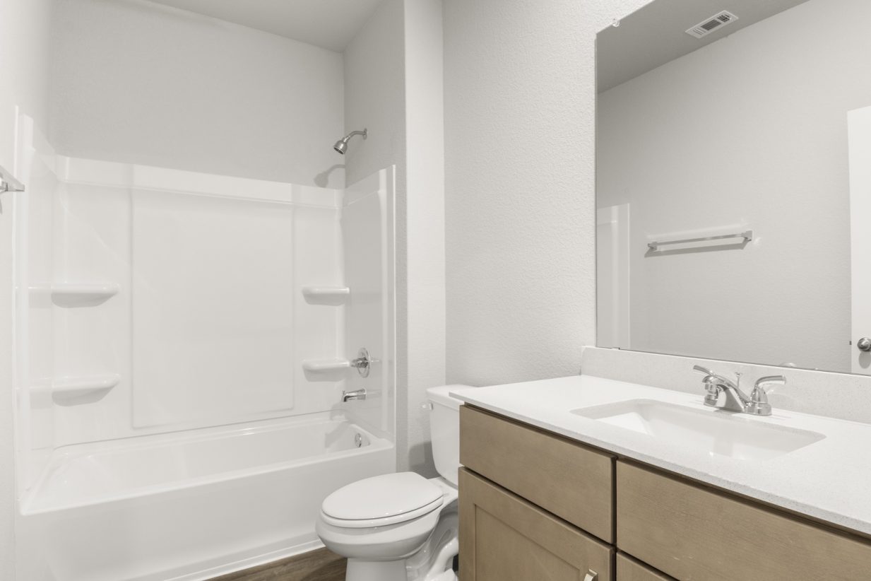 Image of a bedroom with light brown cabinets and a white vanity with a large mirror, and a white vinyl shower and tub