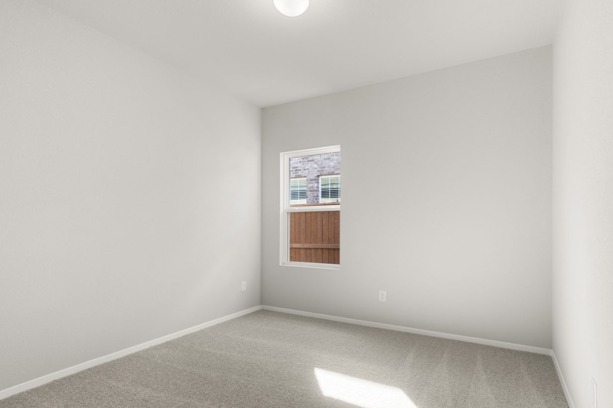Image of a bedroom with tan carpeting and light grey walls with a window