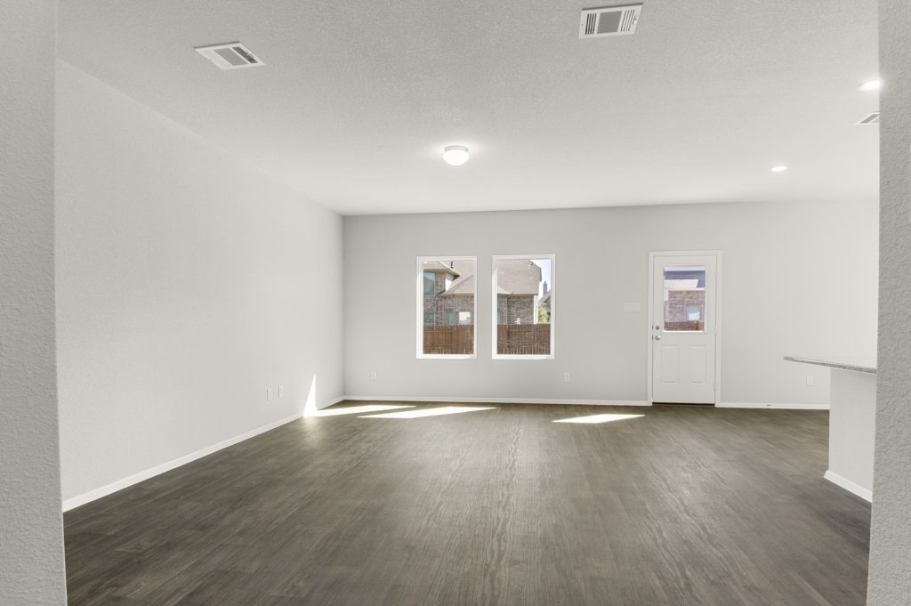 Image of a living room with brown wood-look flooring and light grey walls with windows and a backdoor