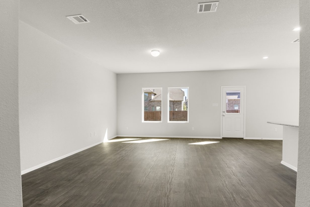 Image of a living room with brown wood-look flooring and light grey walls with windows and a backdoor
