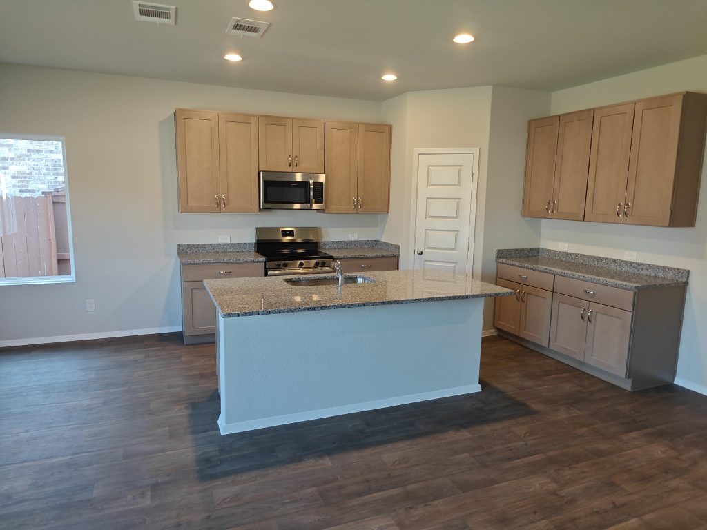 Image of kitchen with light brown cabinets with silestone countertops, stainless steel appliances, and wood look vinyl flooring.