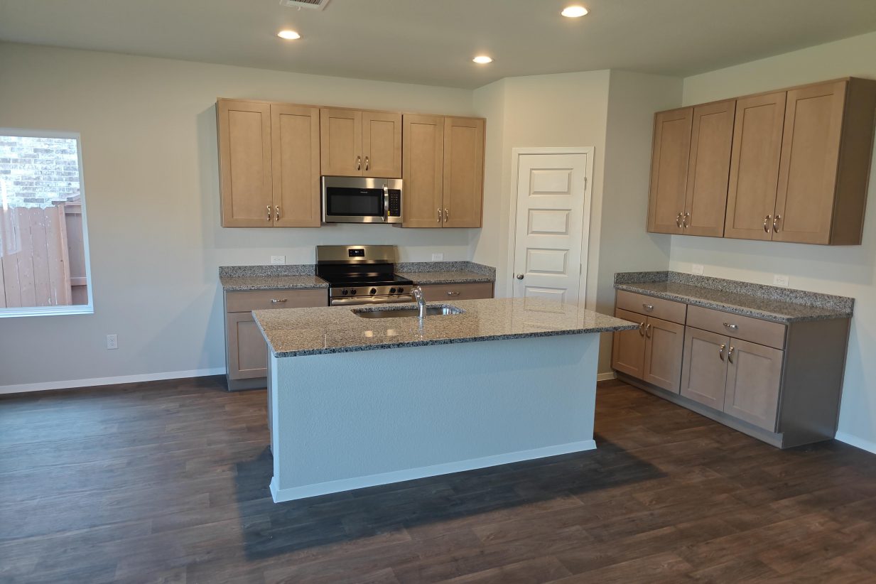 Image of kitchen with light brown cabinets with silestone countertops, stainless steel appliances, and wood look vinyl flooring.