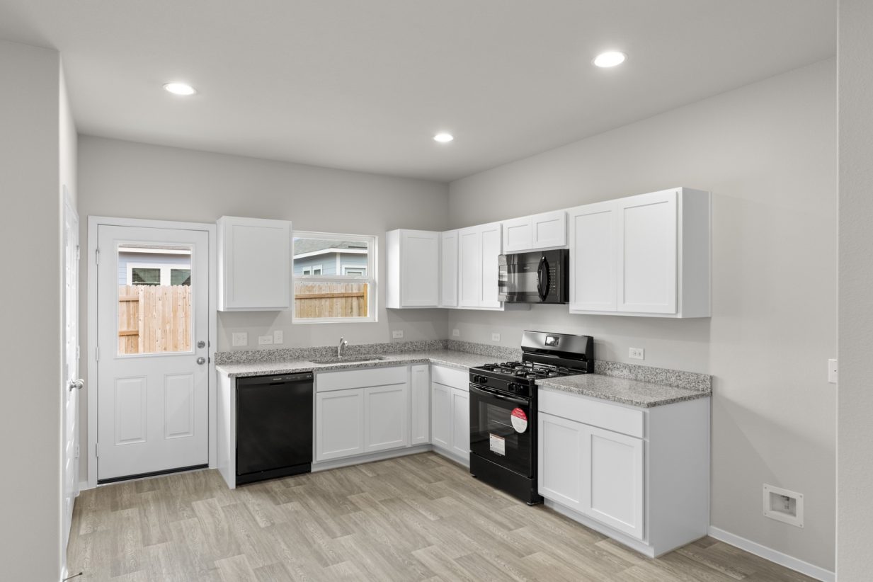 Image of an L-shaped kitchen with white cabinets, black appliances, a white back door and a window above the sink