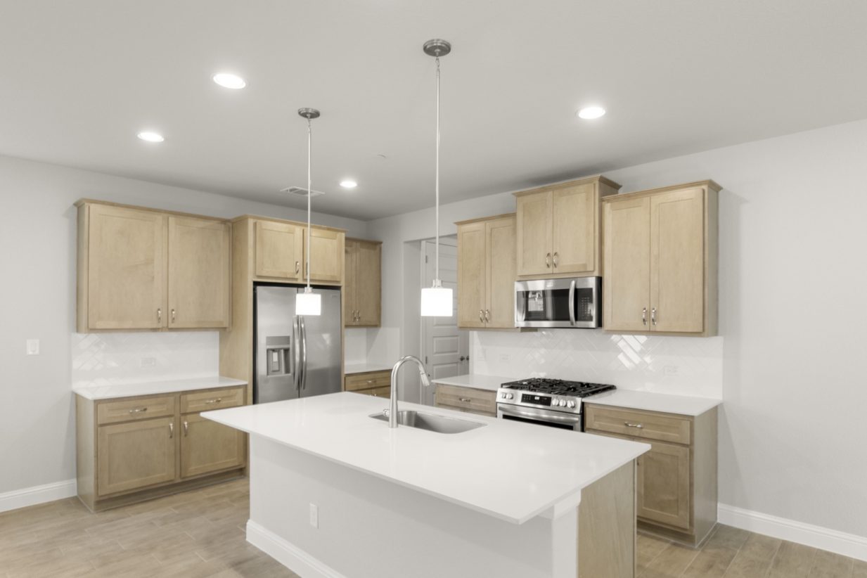 Image of a kitchen with a center island and light brown cabinetry with white backsplash and stainless steel appliances