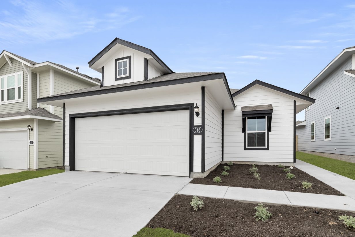 Image of a white one story house with black trim, a white garage, a cement driveway, and a blue sky in the background