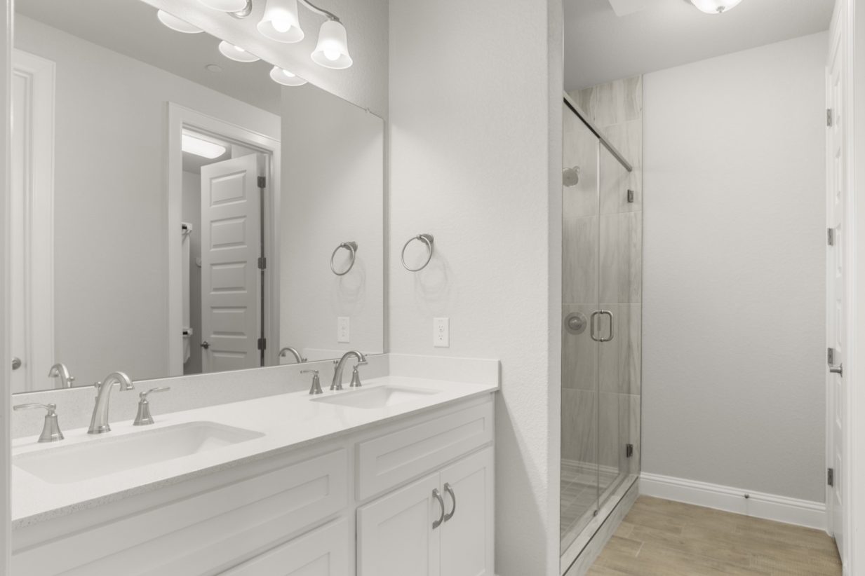 Image of a primary bathroom with white cabinets and jack and jill vanity with a large mirror and walk-in shower