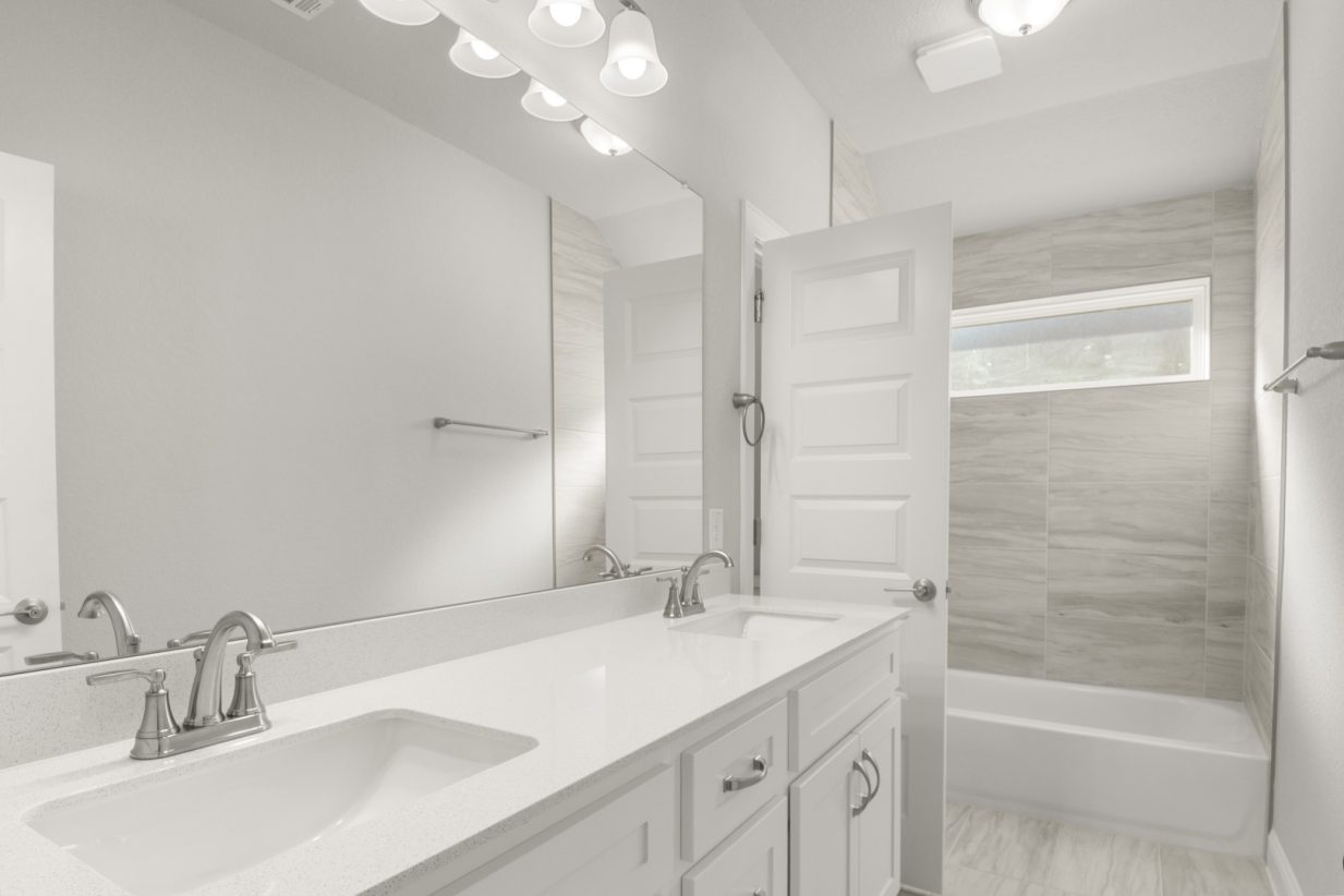 Image of a bathroom with white cabinets and white jack and jill vanity with a large mirror and a shower with tub