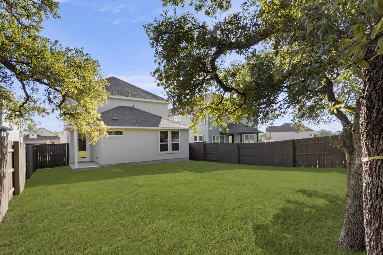 Image of back exterior of a two story home with a large green grass backyard with trees and a wooden fence