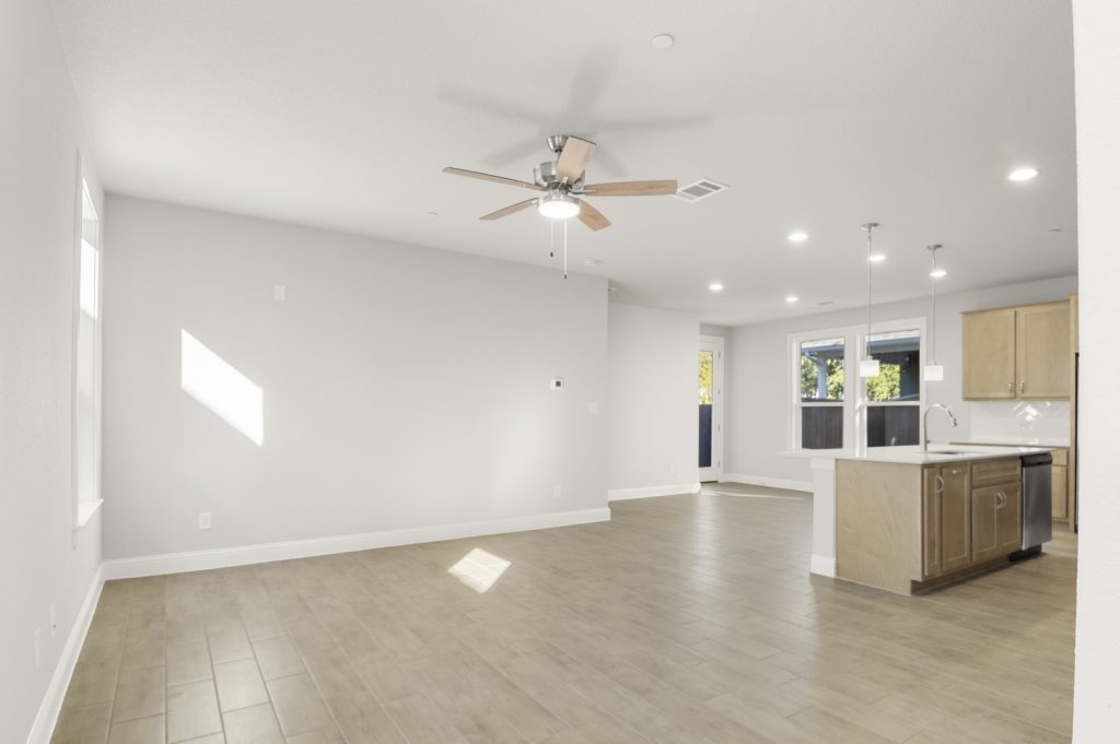 Image of a two story home living room with light wood-like flooring with light grey painted walls and a ceiling fan