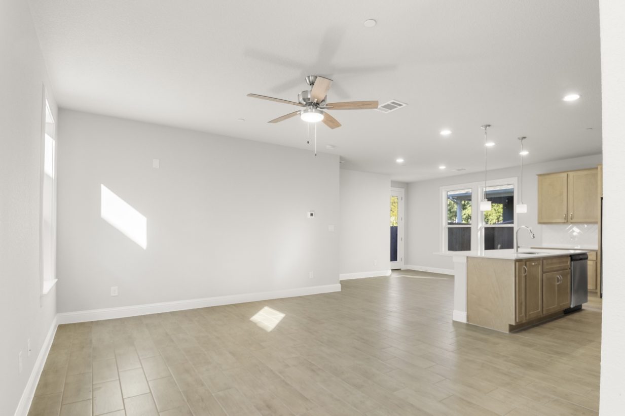 Image of a two story home living room with light wood-like flooring with light grey painted walls and a ceiling fan