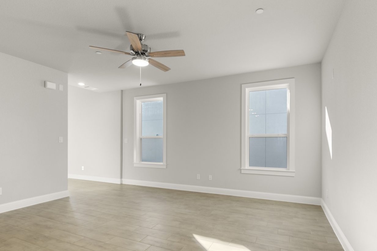 Image of a living room with light brown flooring and light grey painted walls with two windows and a ceiling fan