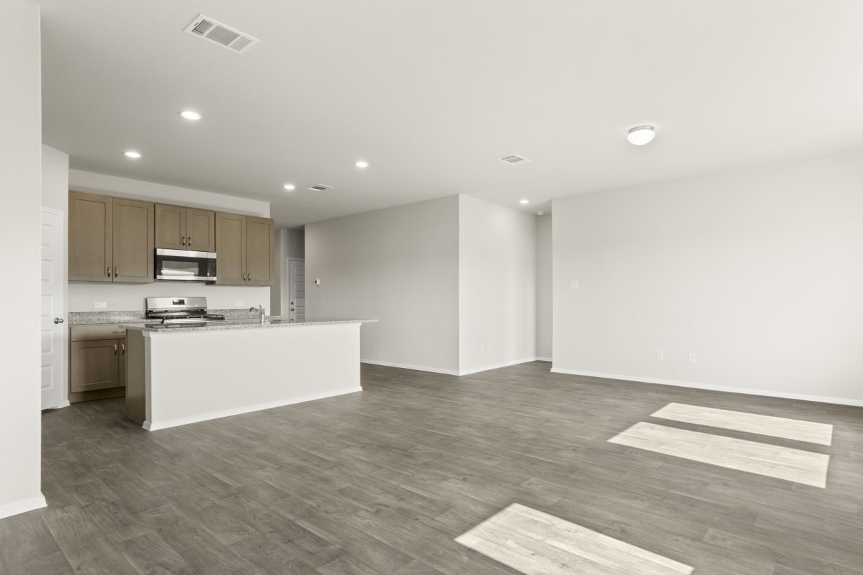 Image of a dining room with dark vinyl flooring, cream walls, and a kitchen with a center island