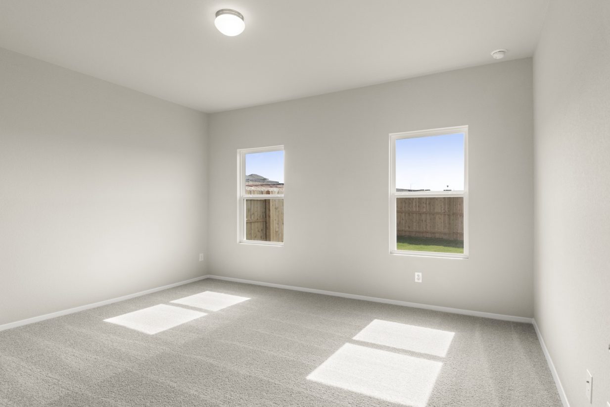 Image of a primary bedroom with tan carpeting, light grey walls and two windows