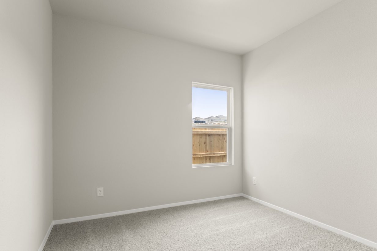 Image of a bedroom with tan carpeting, light grey walls and a window