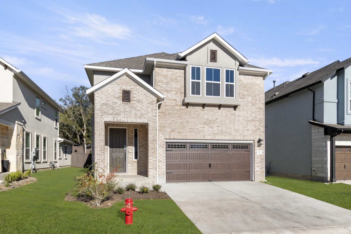 Front exterior of two-story brick house with a brown garage door and a green landscape.