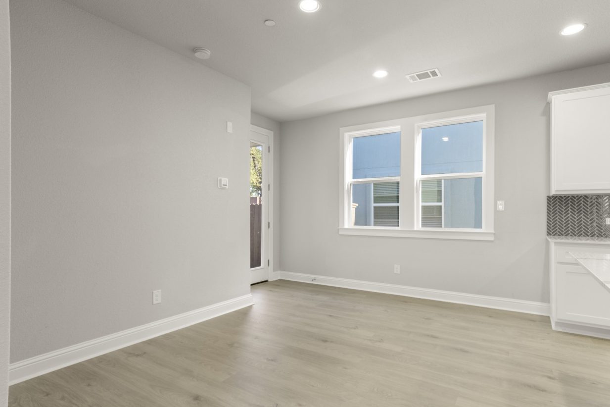 Image of a two story home dining room with light brown flooring and light grey painted walls with a large window