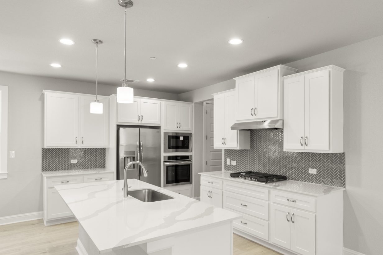Image of a two story home kitchen with white cabinetry and stainless steel appliances with a gas stove and dark grey backsplash