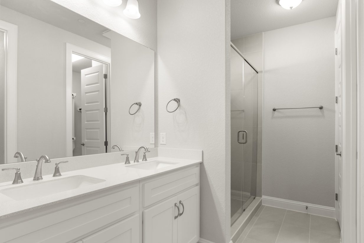 Image of primary with white cabinets and a jack and jill vanity with a large mirror and a walk-in shower
