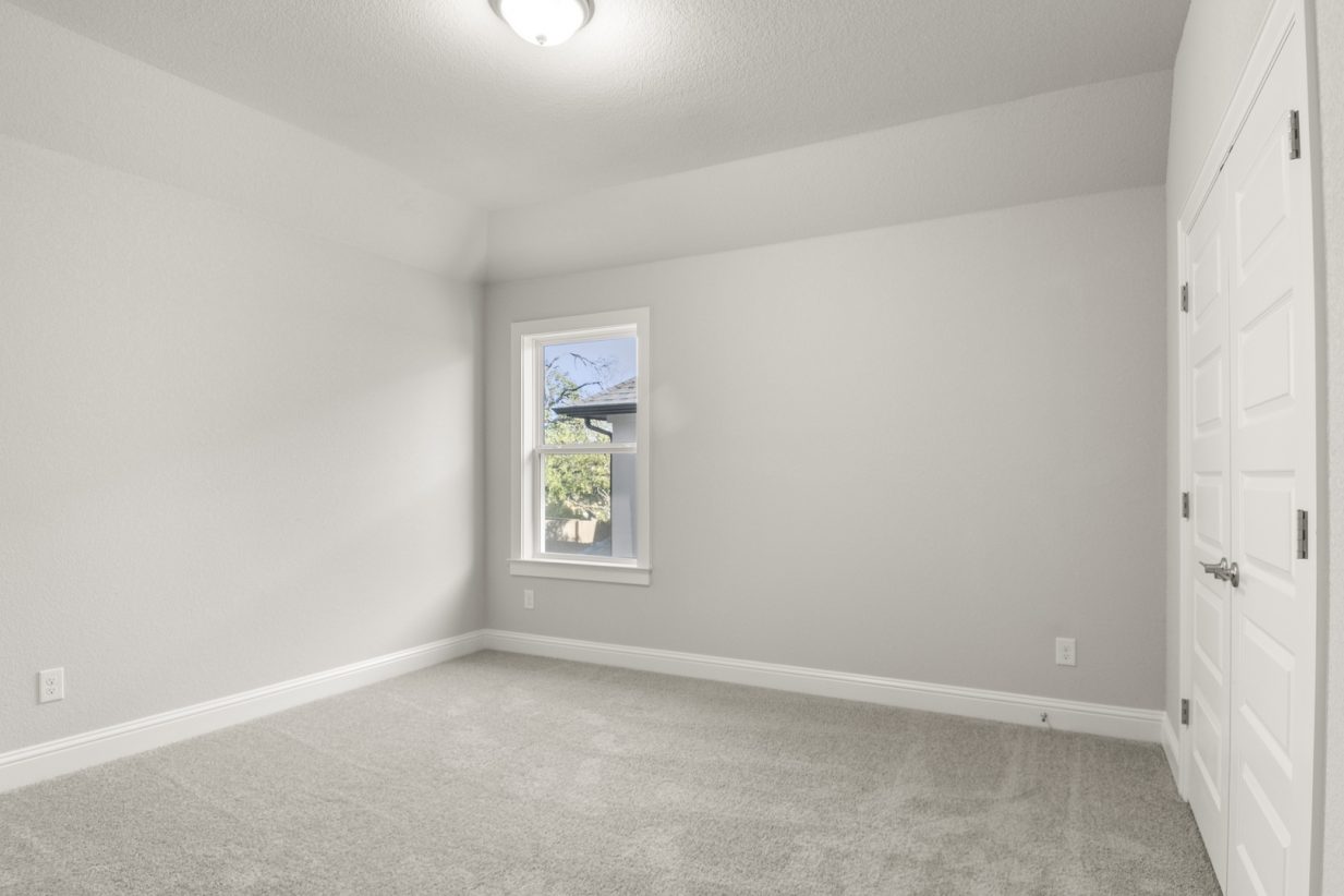 Image of a bedroom with grey carpeting and painted walls with a window and closet