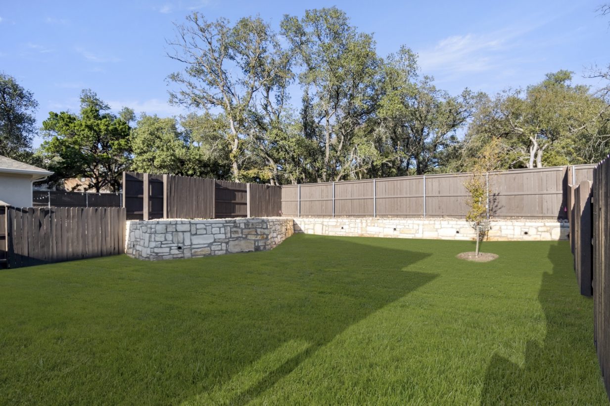 Image of a backyard with green grass and a wooden fence with stone underlining