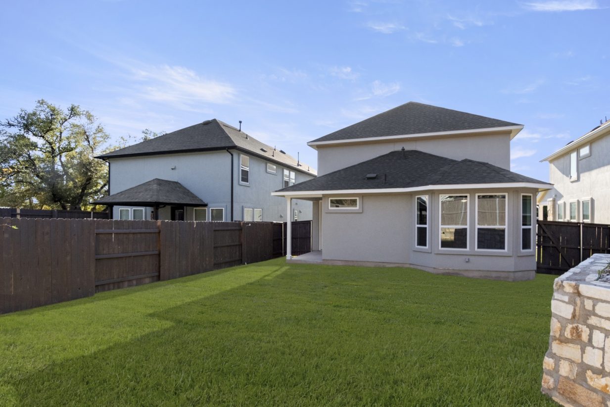Image of the back exterior of a one story home with green grass and a dark brown fence