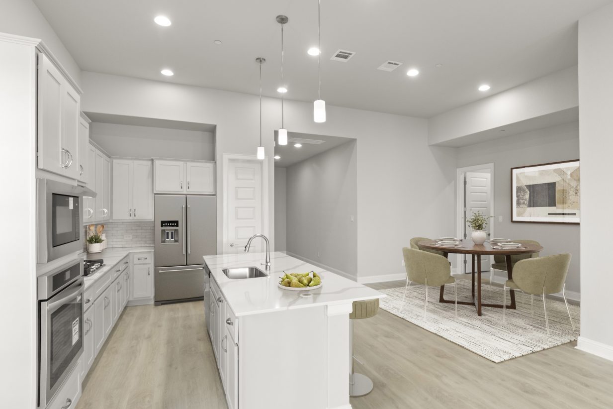 Image of a kitchen and dining room with a dining room rug and round table with dining setting, a stainless steel refrigerator and fruit set on the countertops