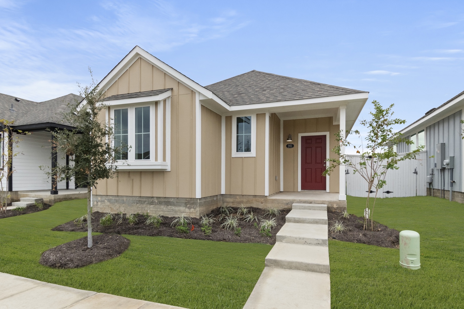 Image of front of yellow single-story house with a red front door, walk way, and green landscape with. a blue sky in the background.