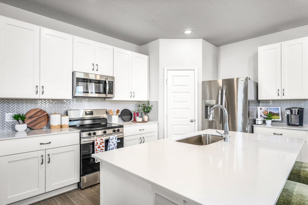 Image of kitchen with white cabinets with white countertops, wood flooring, and a white painted wall.