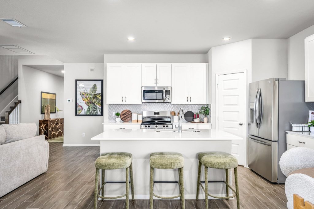 Image of kitchen with white cabinets with white countertops, wood flooring, and a white painted wall.