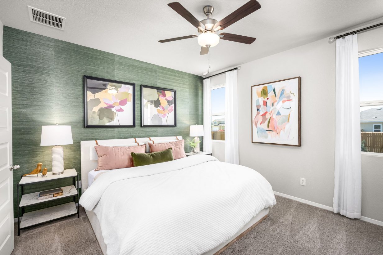 Image of primary bedroom with tan carpet, green accent walls, a window, a bed with white bedding, pink and dark blue pillow, a brown ceiling and colorful wall art.