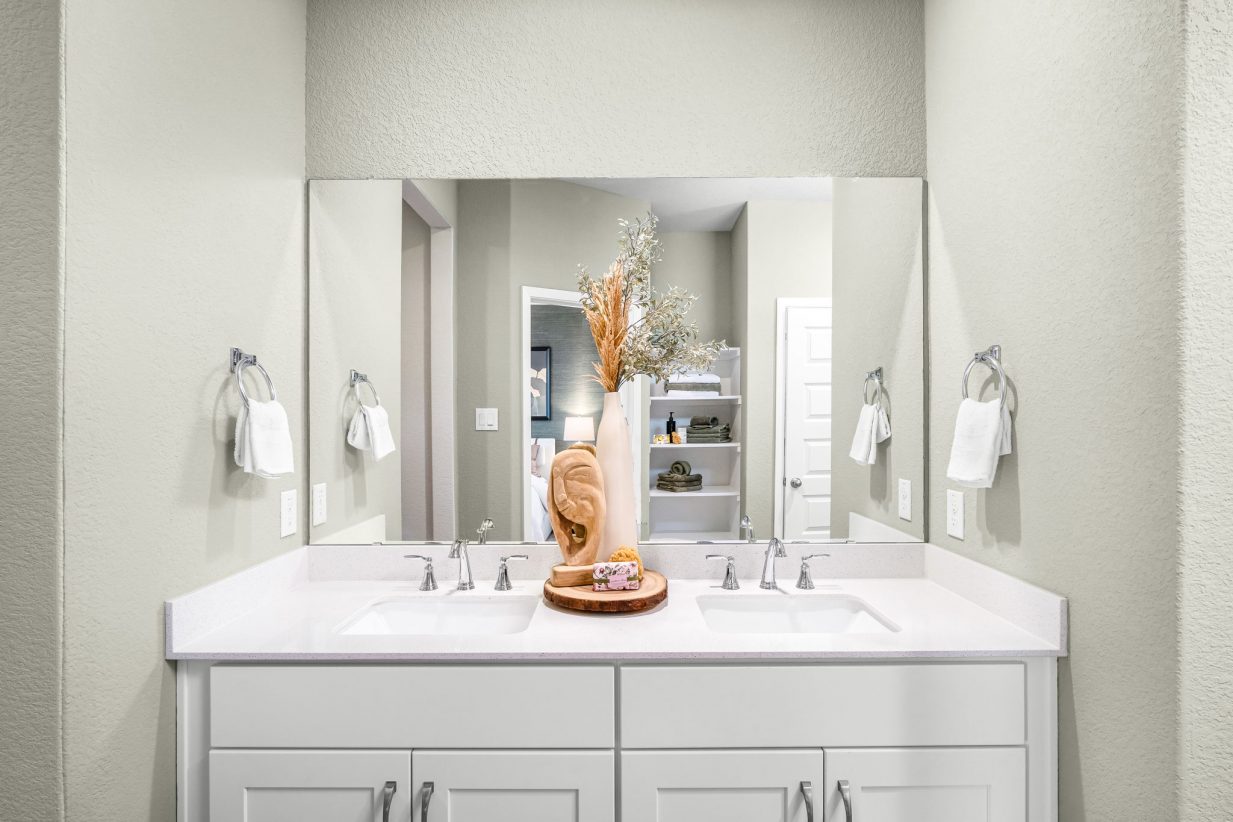Image of the primary bathroom with light green walls, white vanity with white countertops.