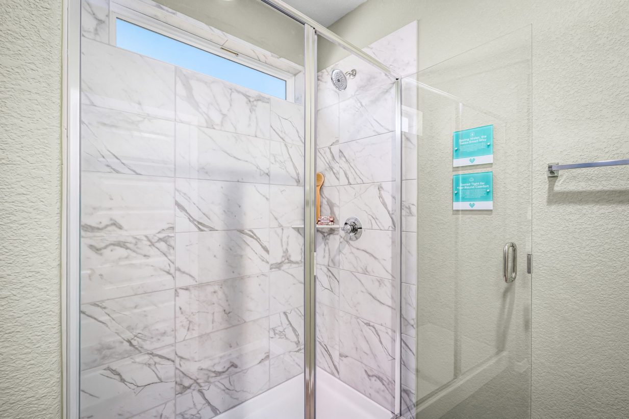 Image of bathroom with a glass shower with marbled tiled walls, and light green painted walls.
