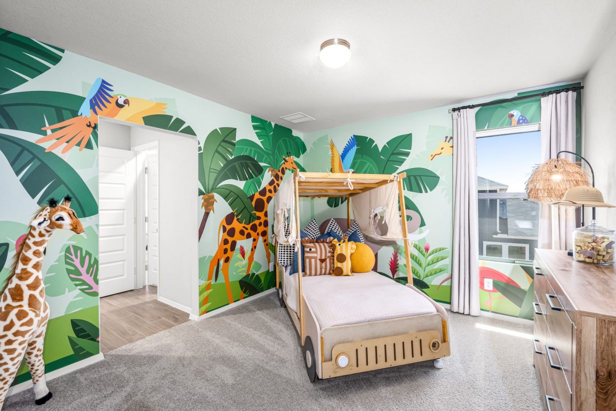 Image of bedroom with safari leaves and animals painted on the walls, tan carpet, a child's bed with wheels and a white covering, wooden dresser, and a giraffe.