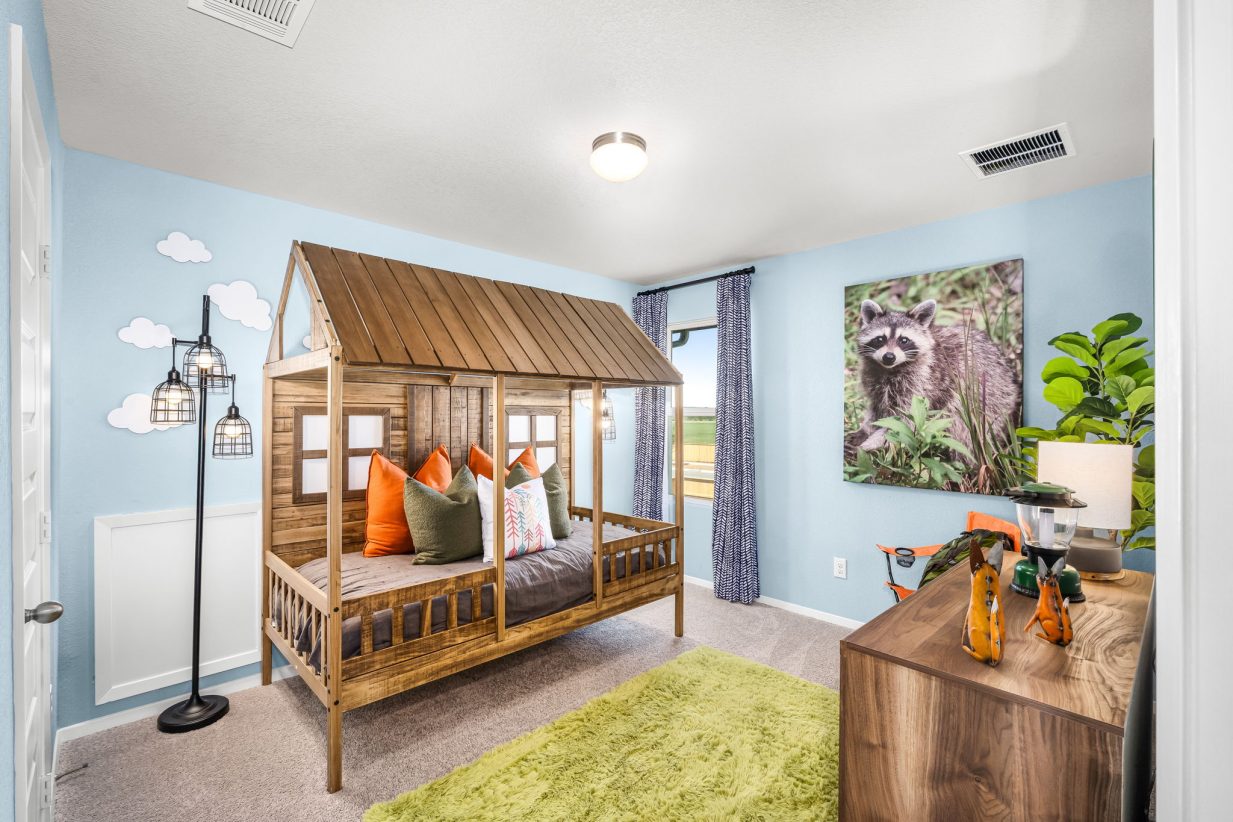 Image of children's bedroom with a camping theme with tan carpet, a light green rug, bed that resemebles a cabin, blue painted walls,and a raccoon art.