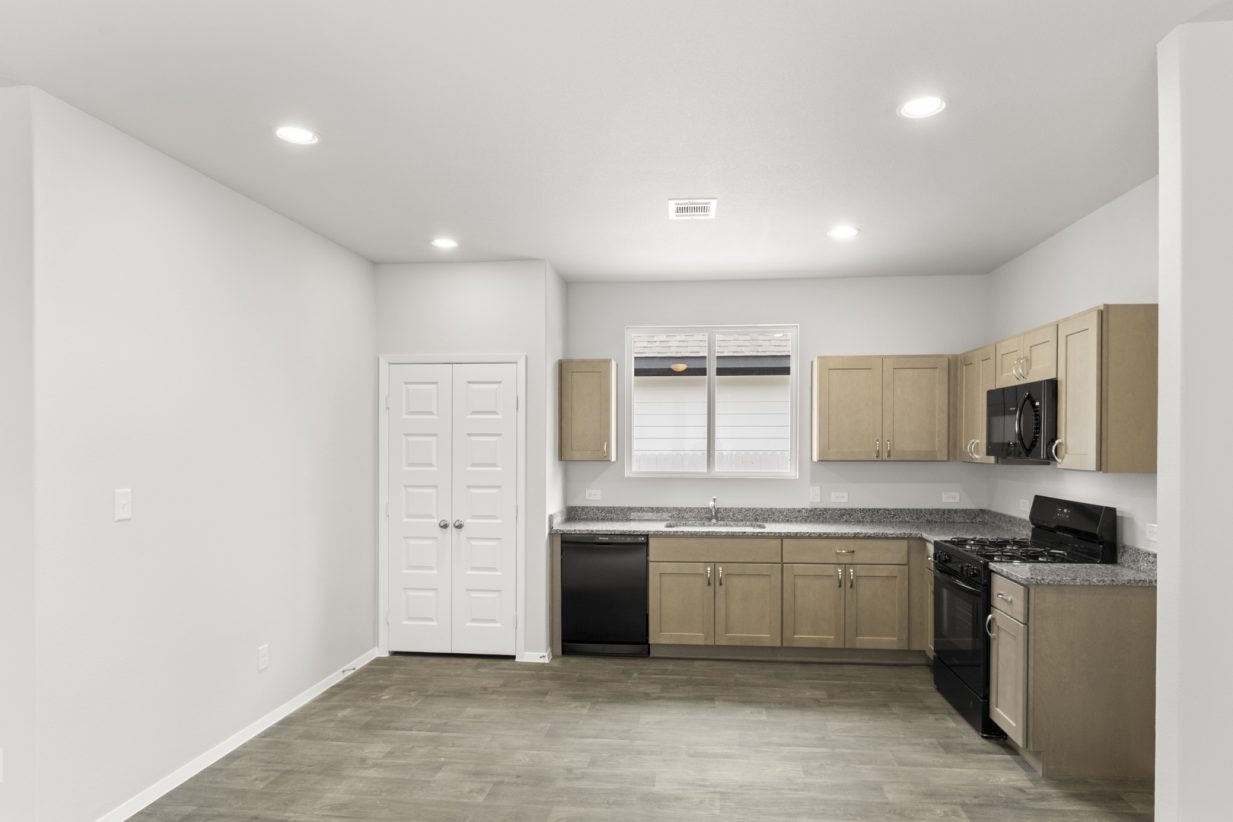 Image of a L-shaped kitchen with granite countertops, black appliances, brown cabinetry, brown vinyl flooring and light grey walls