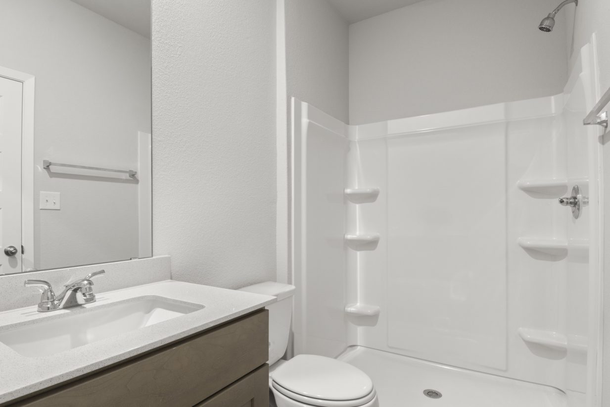 Image of a primary bathroom with a white vinyl shower and a white vanity with brown cabinets and a large mirror