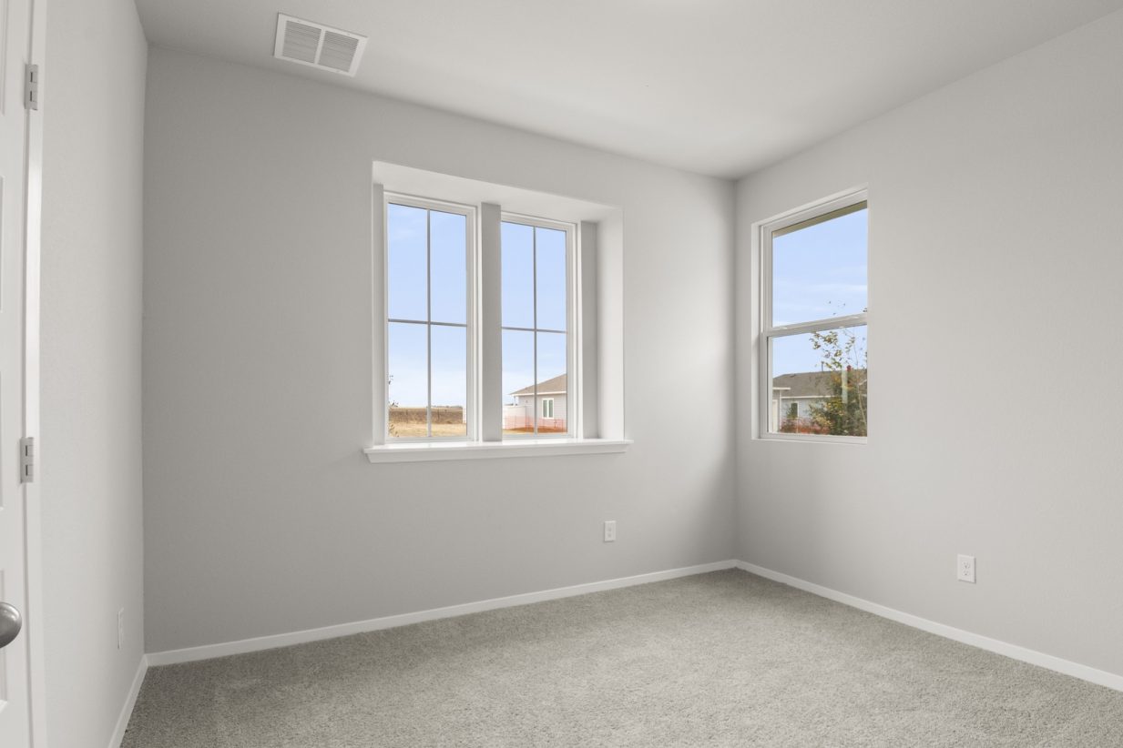 Image of a bedroom with tan carpeting and light grey walls with windows