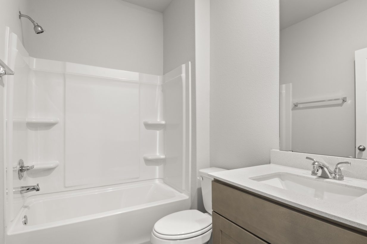 Image of a bathroom with a white vinyl shower and tub, a white vanity with brown cabinets and a large mirror