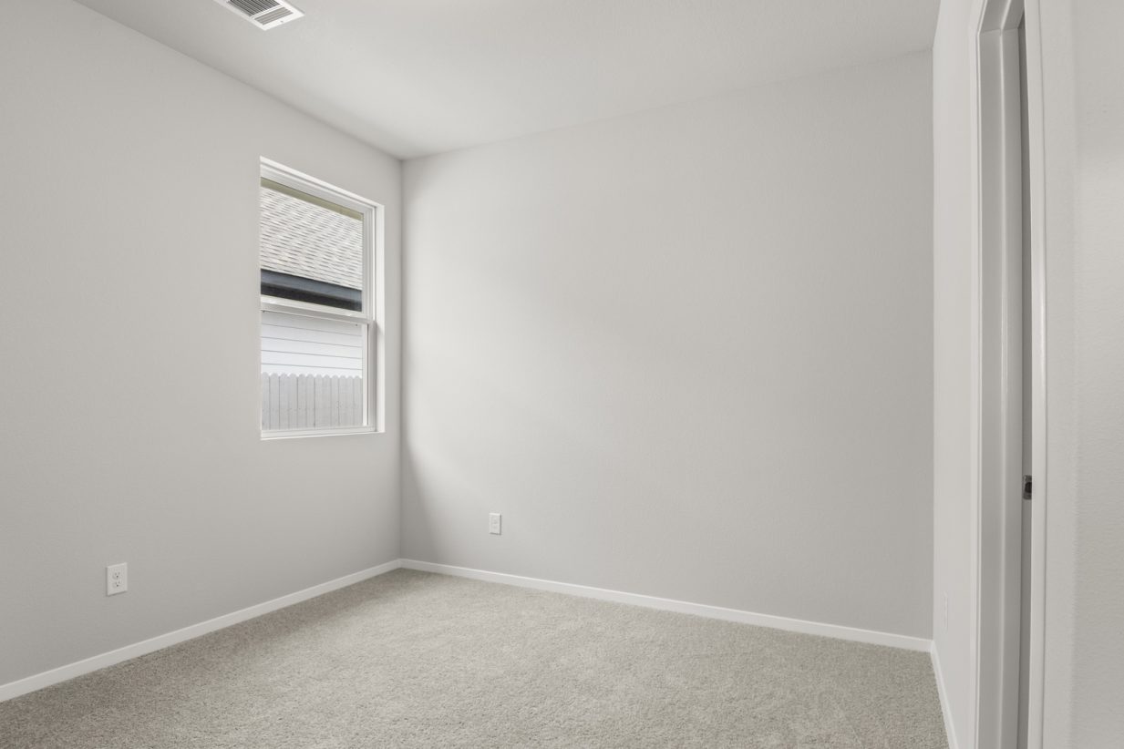 Image of a bedroom with tan carpeting and light grey walls with a mirror