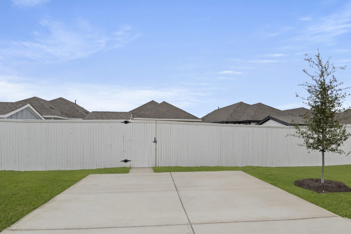 Image of a back exterior of a one story home cement driveway with a white fence
